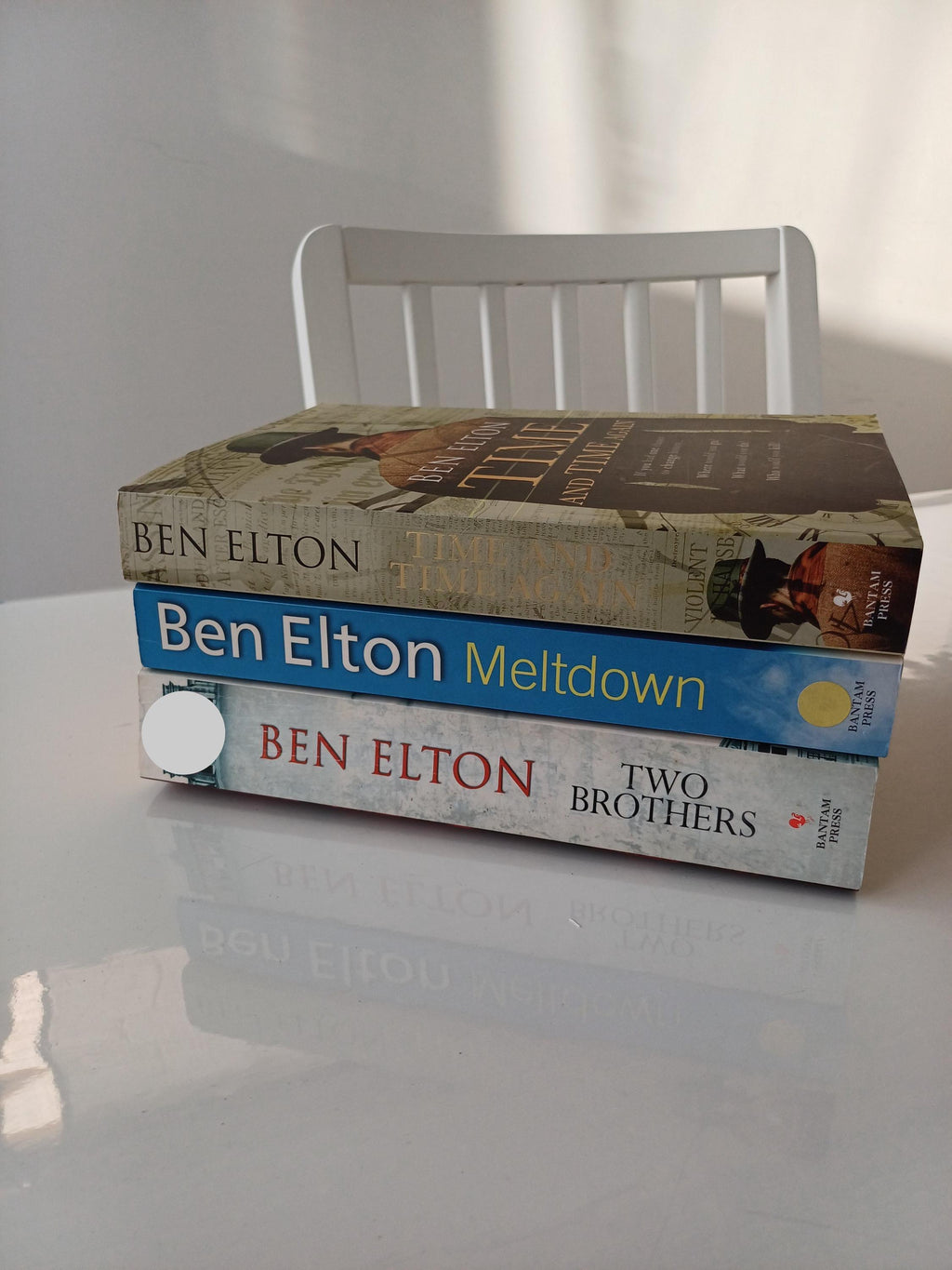Three books by Ben Elton on a white surface with a blurred background
