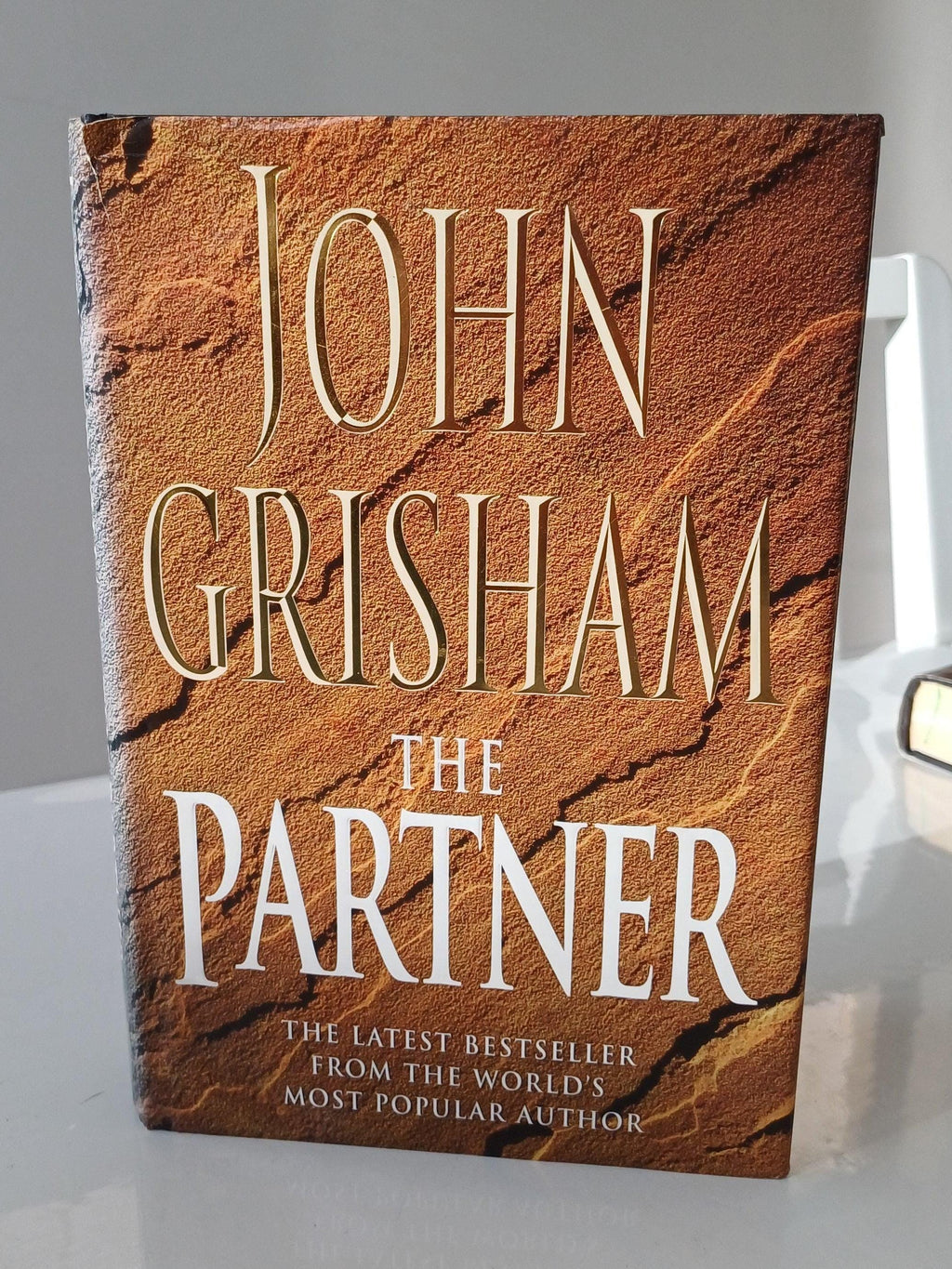 Book titled 'The Partner' by John Grisham on a white surface with a gray background
