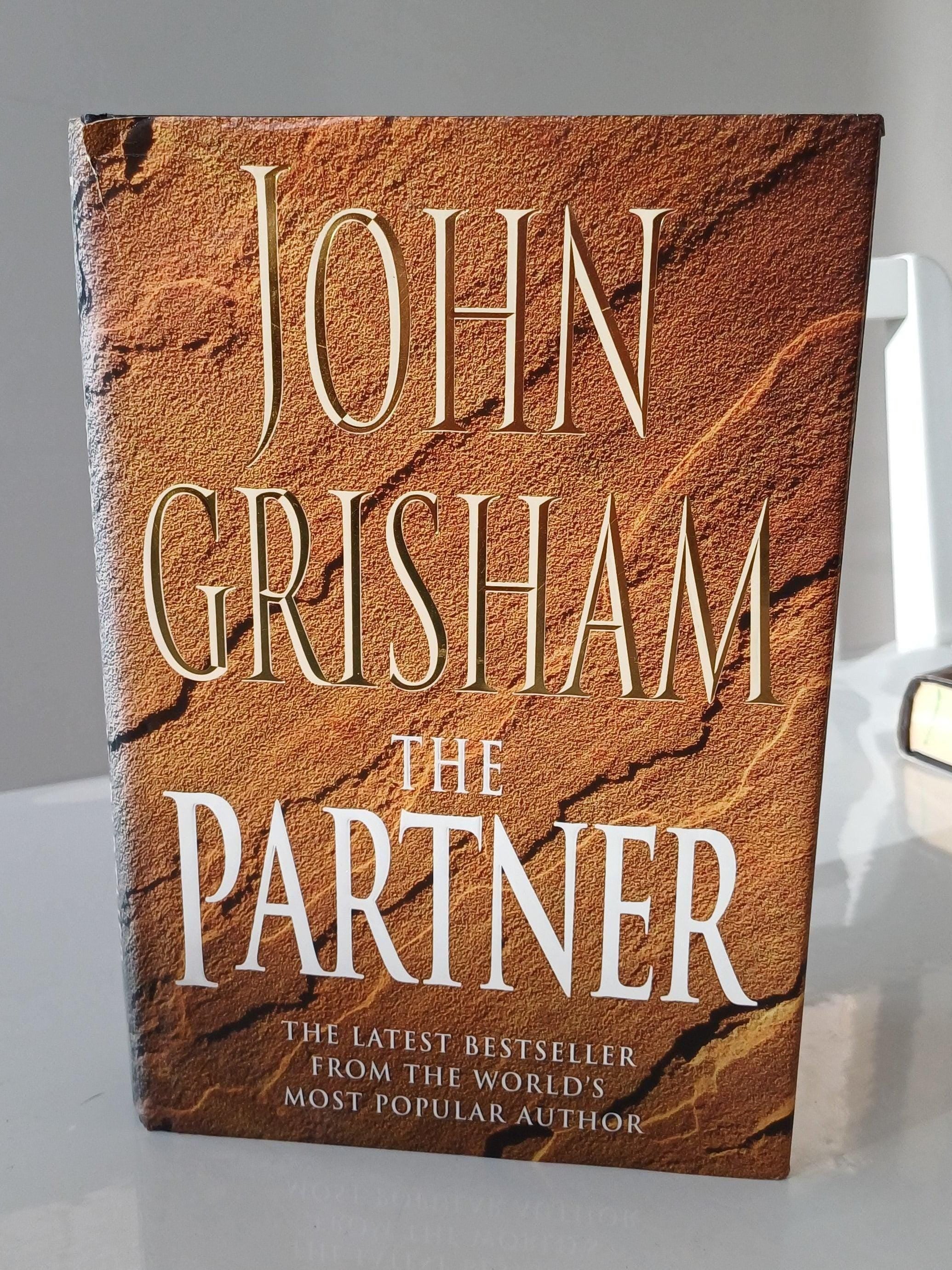 Book titled 'The Partner' by John Grisham on a white surface with a gray background